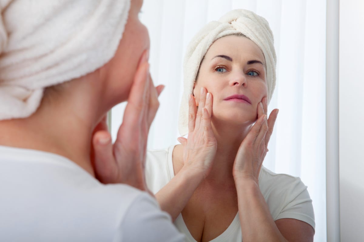 Middle aged woman touching face and lifting skin in mirror