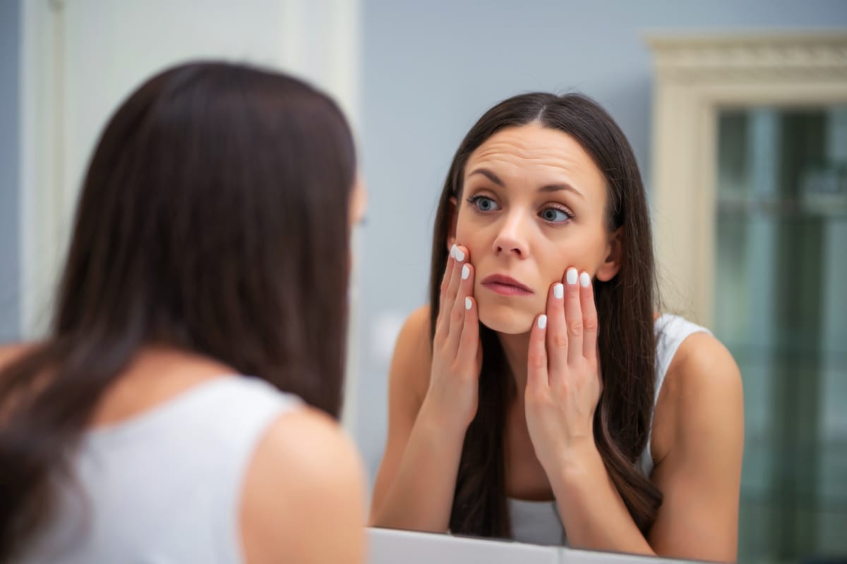 Young woman looking at wrinkles in mirror after she stopped getting Botox injections