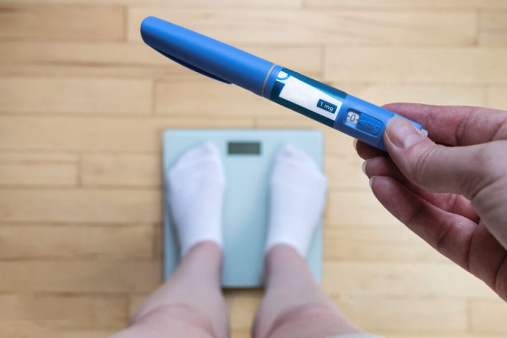 Close up of hand holding weight loss medication cartridge while standing on a scale